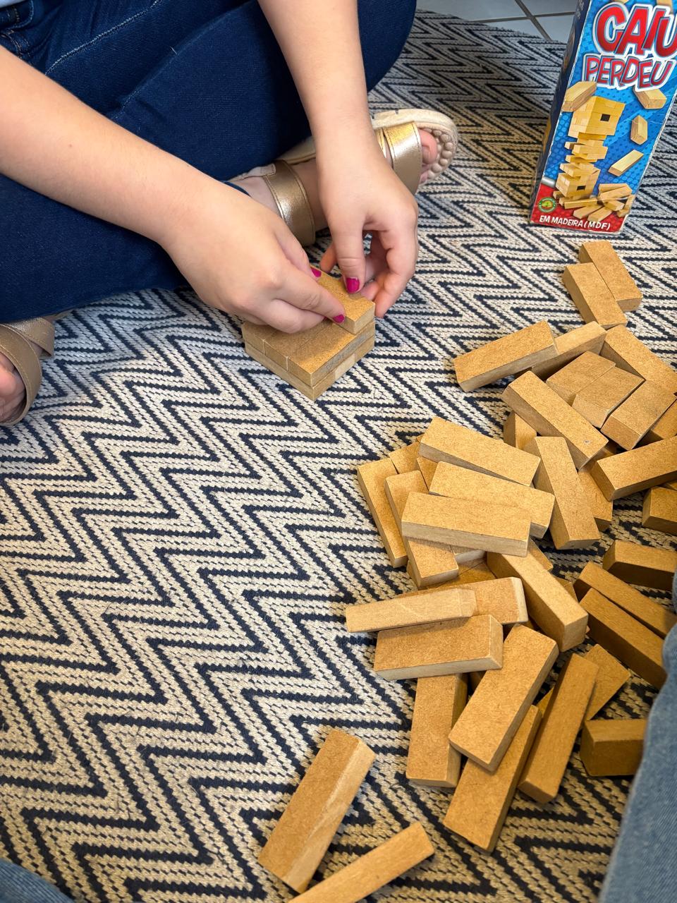 Criança montando uma torre com blocos de madeira durante sessão de terapia lúdica